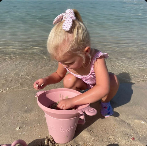 Scrunch Panner (Beach Sieve) - Dusty Rose, child playing on beach, bucket also visible 